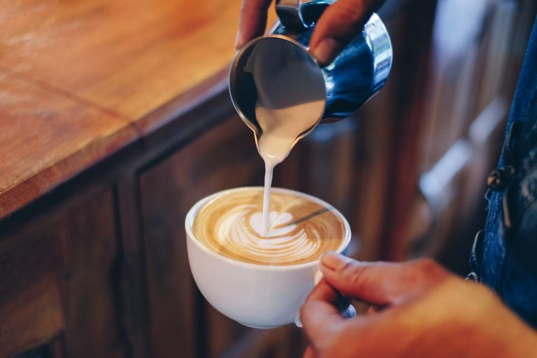 Hand barista pouring milk on coffee latte flower shape in white cup