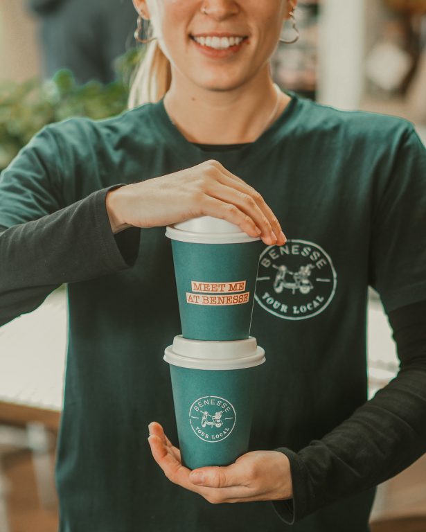 Image of a lady holding two takeaway coffees, one on top of the other