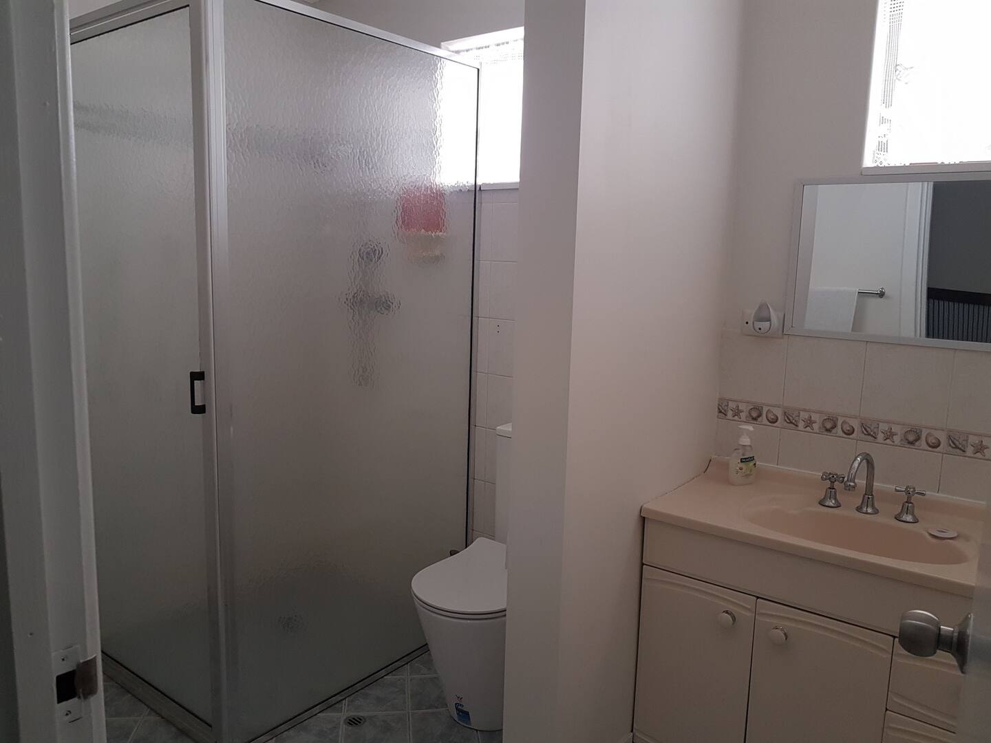 An image of an ensuite bathroom, including a sink, mirror, toilet and walk-in shower.