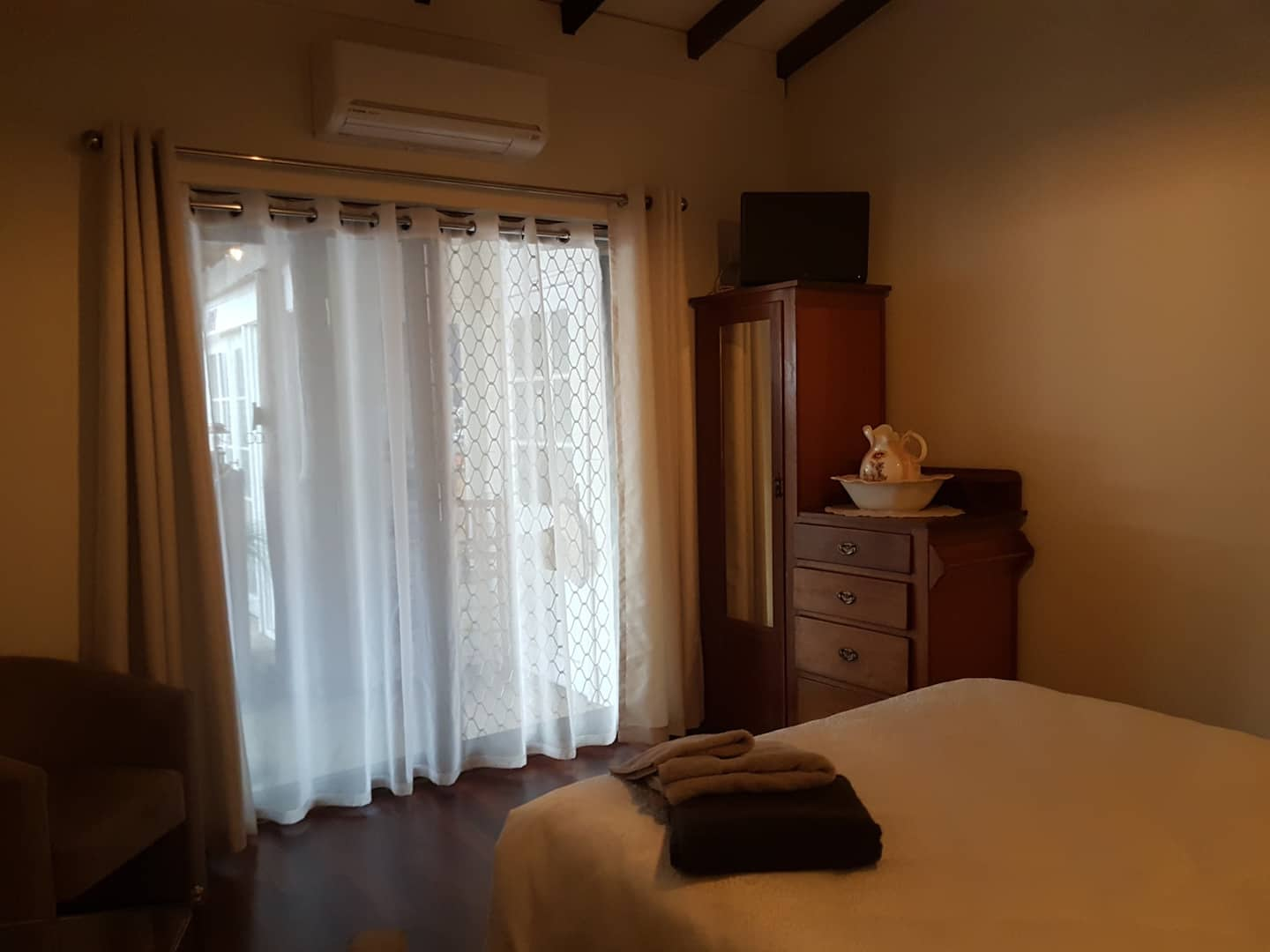 Bedroom from the point of view of the bed, looking out to a large window and sliding door with white curtains.