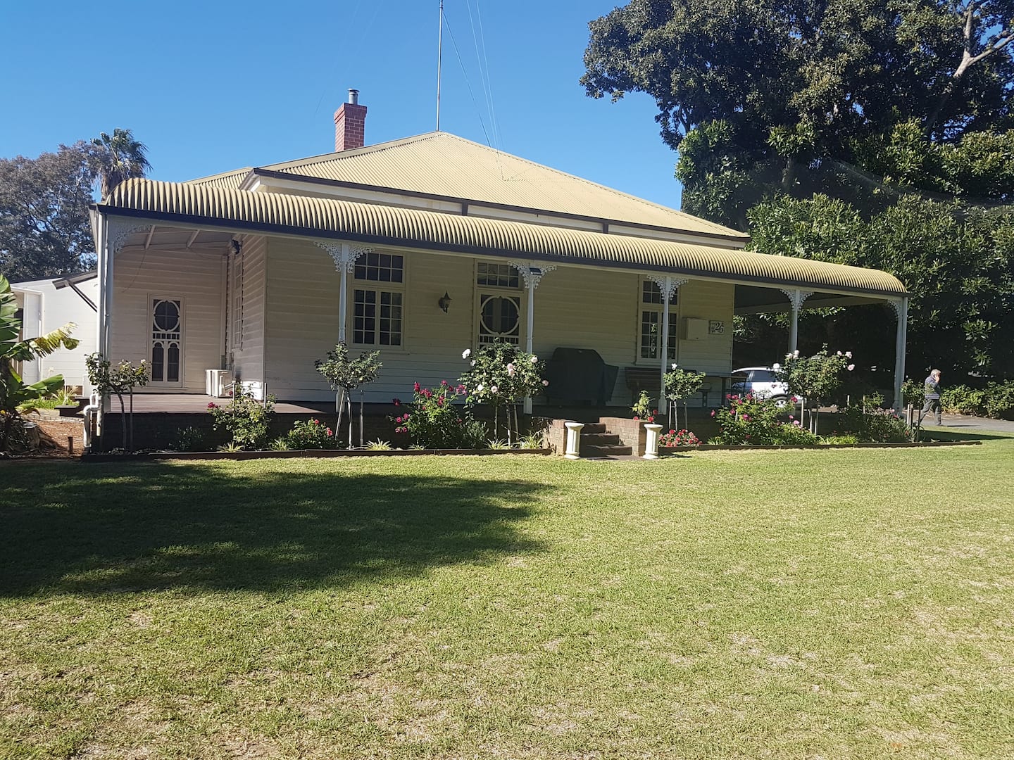 Exterior of the property with a large lawn and three steps leading up to a wooden verandah.