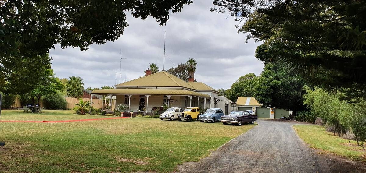 Exterior of the property with a red carpet running across the large lawn and up to the door. Four vintage cars are parked in the front yard.