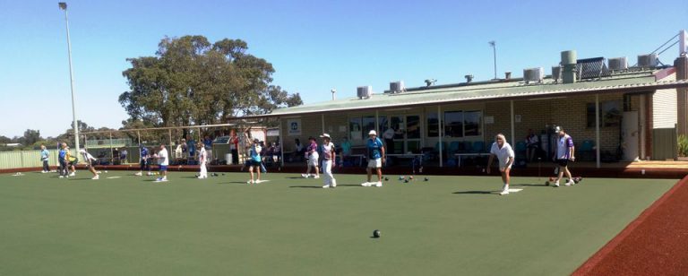 Photo of a group of people playing lawn bowls on a green flat grass area at a bowling club