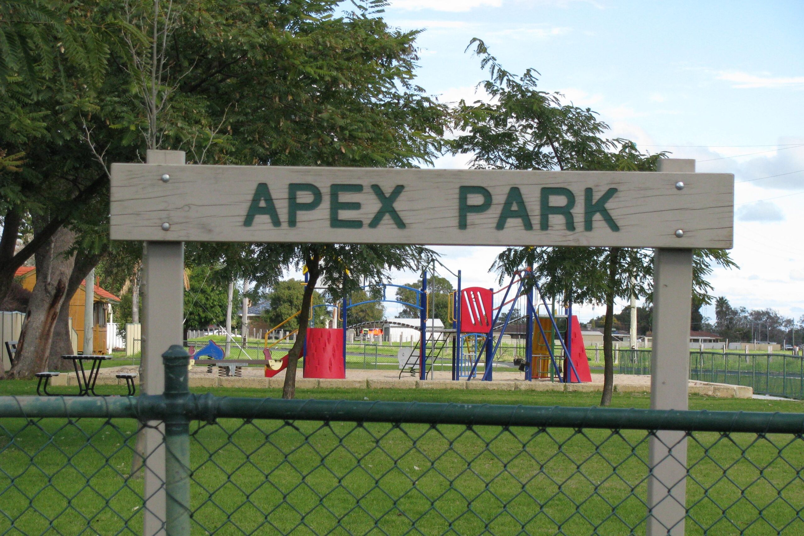 Image of the Apex Park sign and i the background is the playground