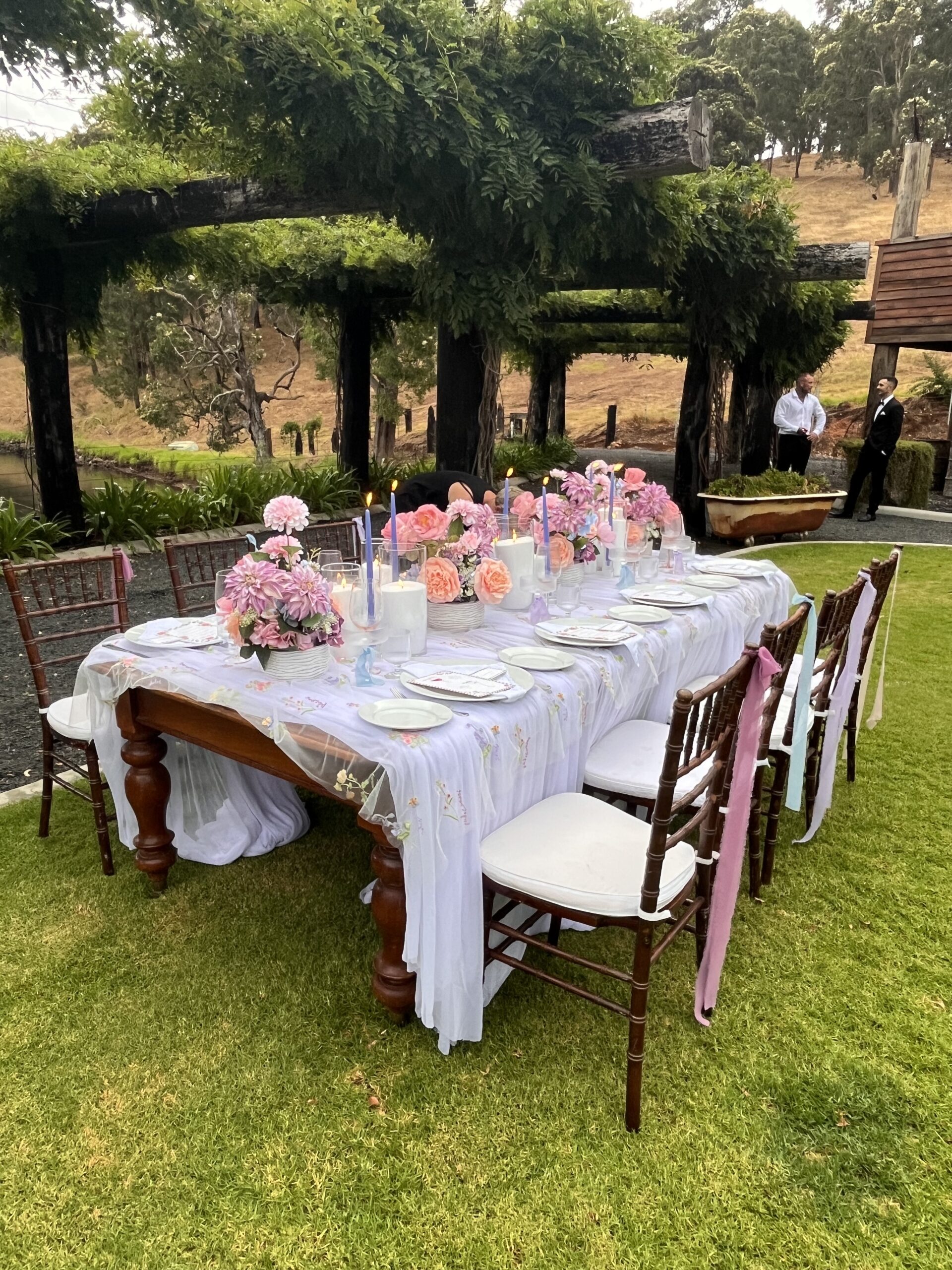 Image of a table setup with pink flowers along the middle and a white table cloth