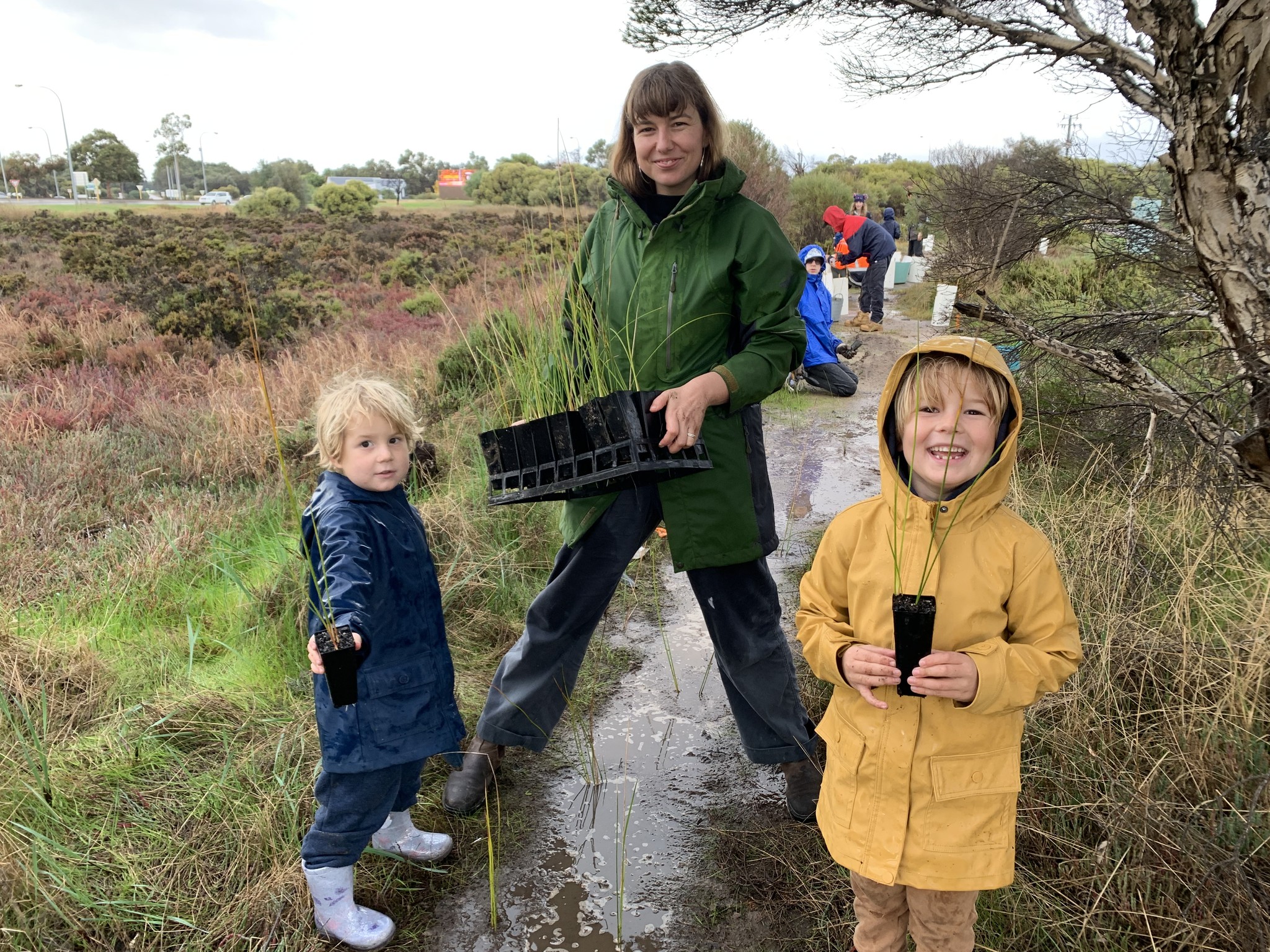 Image of a lady and two kids gardening in wet weather