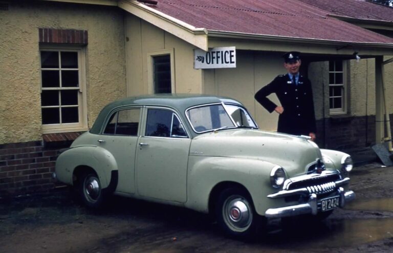 Old photo of policeman standing outside police station with vintage car