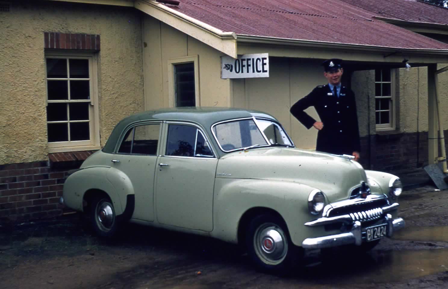 Old photo of policeman standing outside police station with vintage car